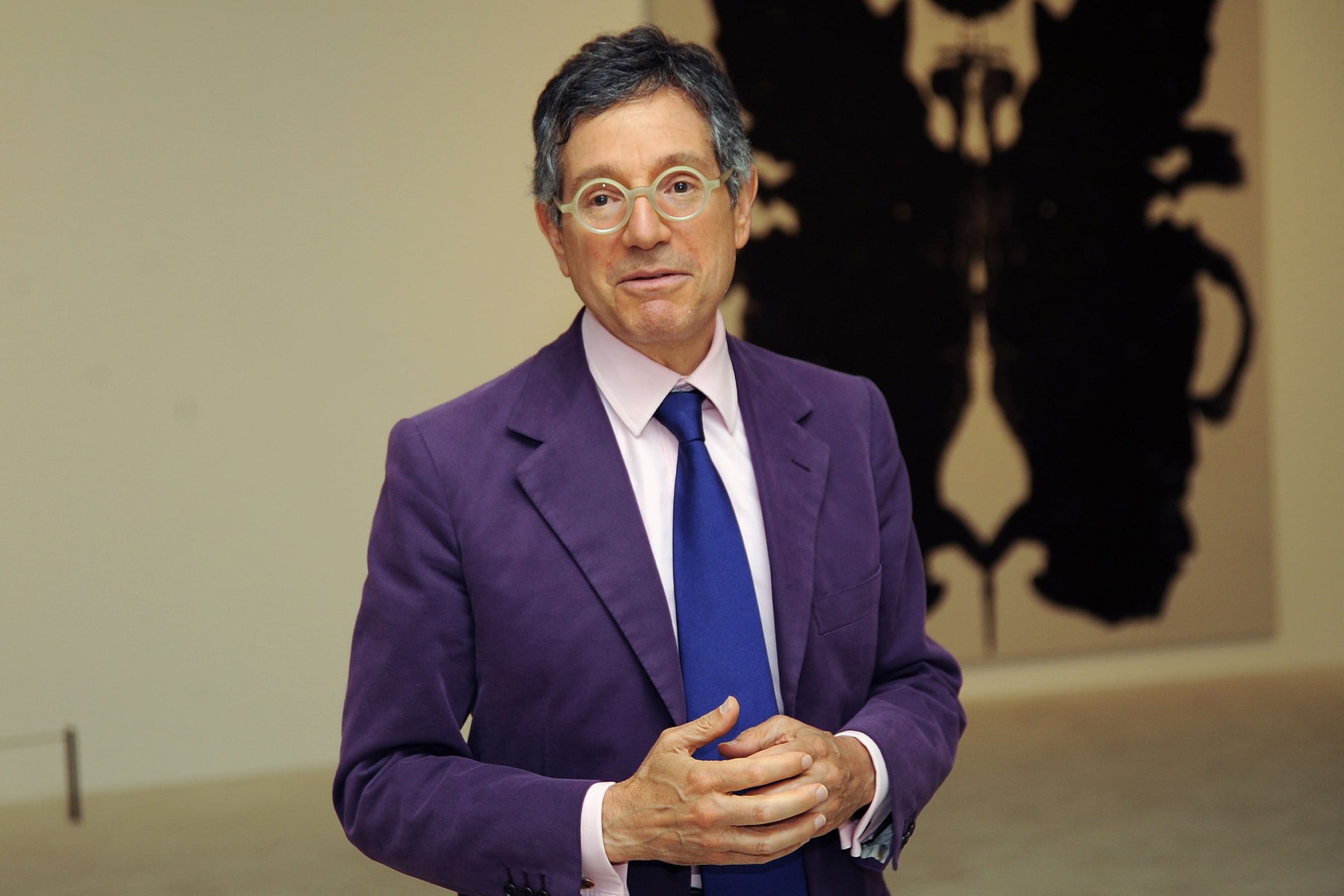 Man in a purple suit and blue tie standing in a gallery with abstract art in the background.