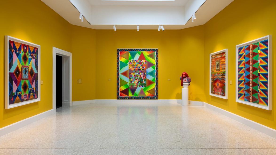 Brightly colored abstract paintings in a modern art gallery with yellow walls and a central skylight.