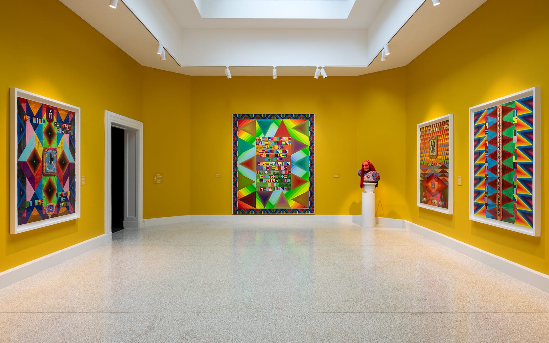 Brightly colored abstract paintings in a modern art gallery with yellow walls and a central skylight.
