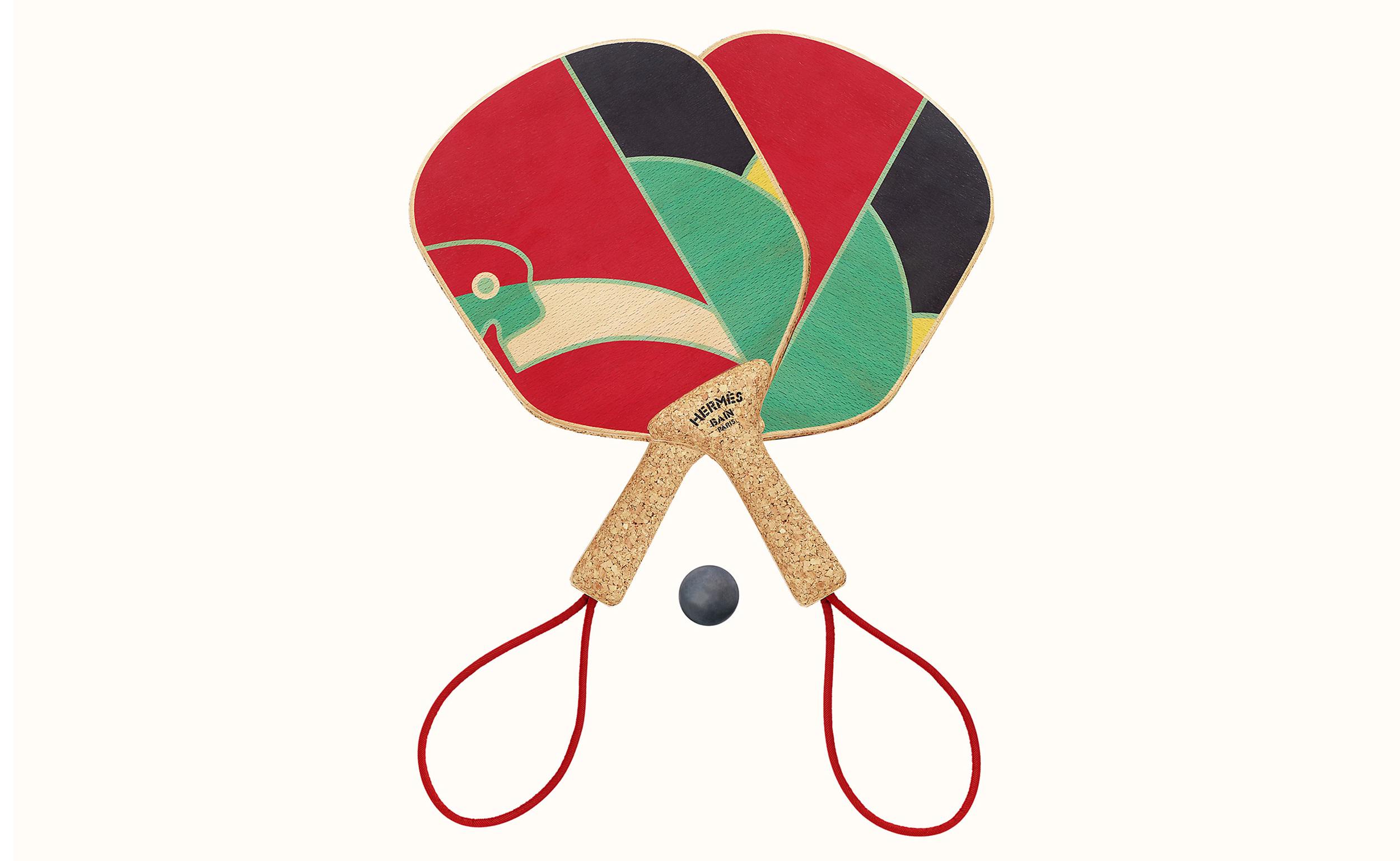 Colorful traditional wooden paddles with abstract patterns and a small black ball against a plain background.