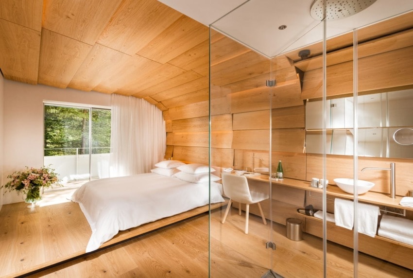 Modern bedroom with wooden walls and floor, glass shower, and a large window with natural light.