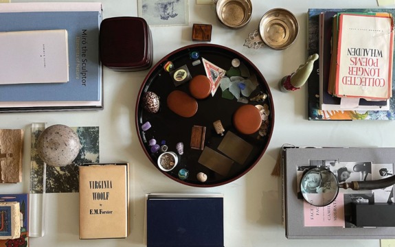 Assorted books and objects, including stones, boxes, and ornaments, arranged on a tabletop with a circular tray in the center.
