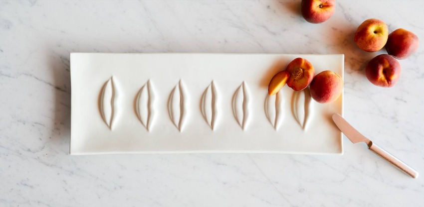 White rectangular plate with indentations, peaches, and a knife on marble surface.