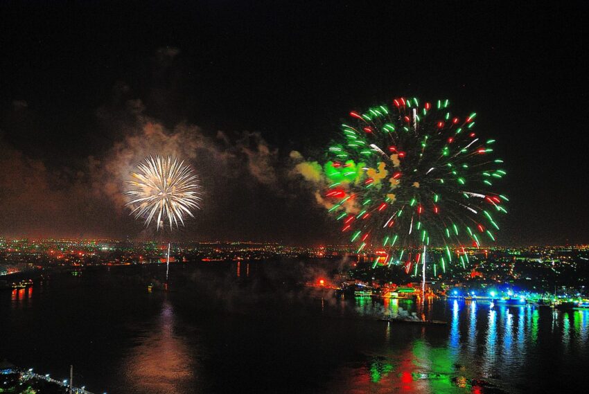 Colorful fireworks illuminate the night sky over a cityscape reflecting on the water.