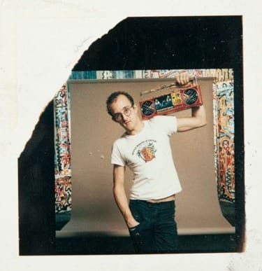 Person holding a boombox on shoulder, standing in front of colorful graffiti background.