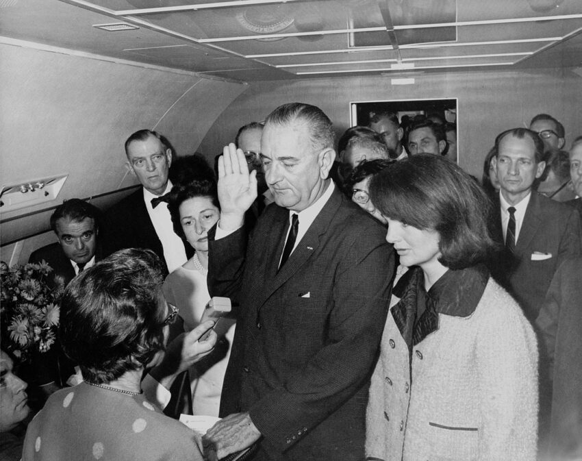A man taking the oath of office aboard an airplane, surrounded by onlookers.