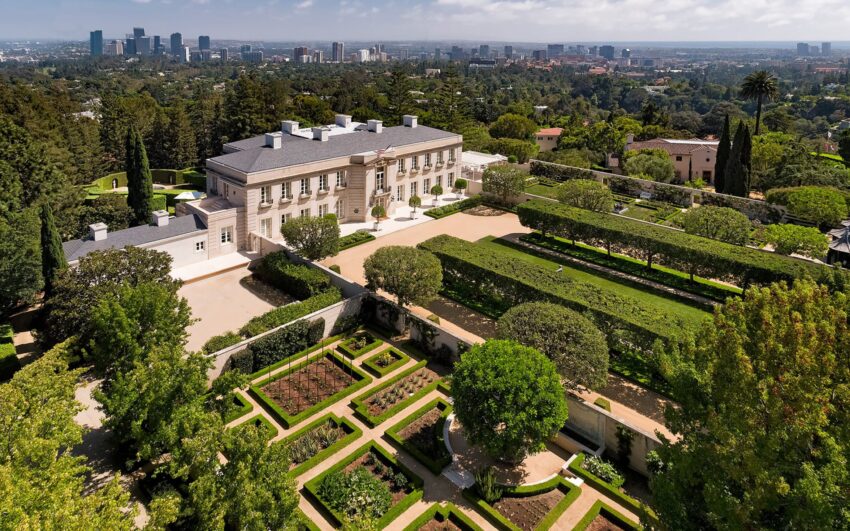 Aerial view of a large mansion surrounded by meticulously landscaped gardens and greenery.