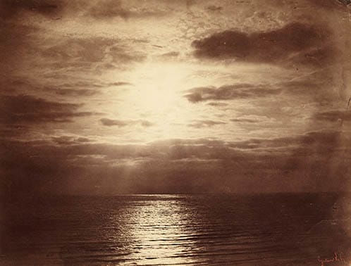 Vintage sepia-toned photo of a serene ocean view with calm waters reflecting sunlight breaking through a cloudy sky.