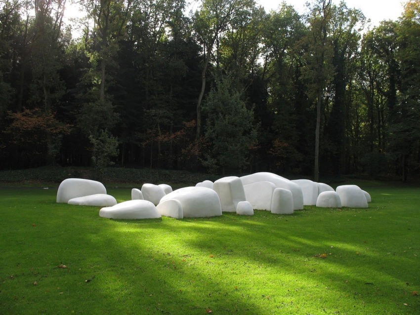 Large white stone sculptures on green grass surrounded by trees in a forest setting.