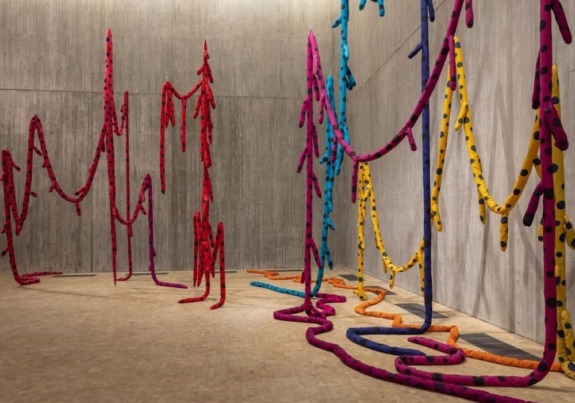 Colorful fabric installations with polka dots hanging in a modern concrete gallery space.