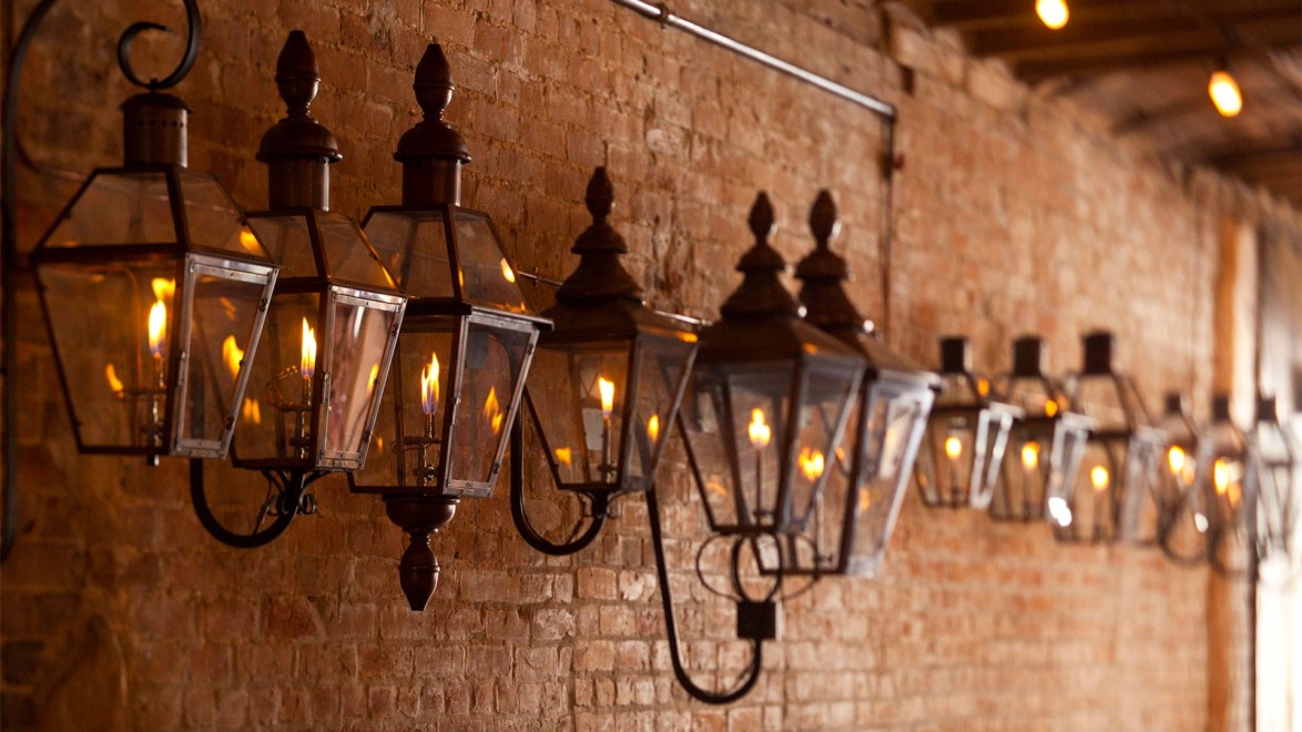 Row of vintage lanterns with warm glow lined along a rustic brick wall, creating a cozy and inviting atmosphere.