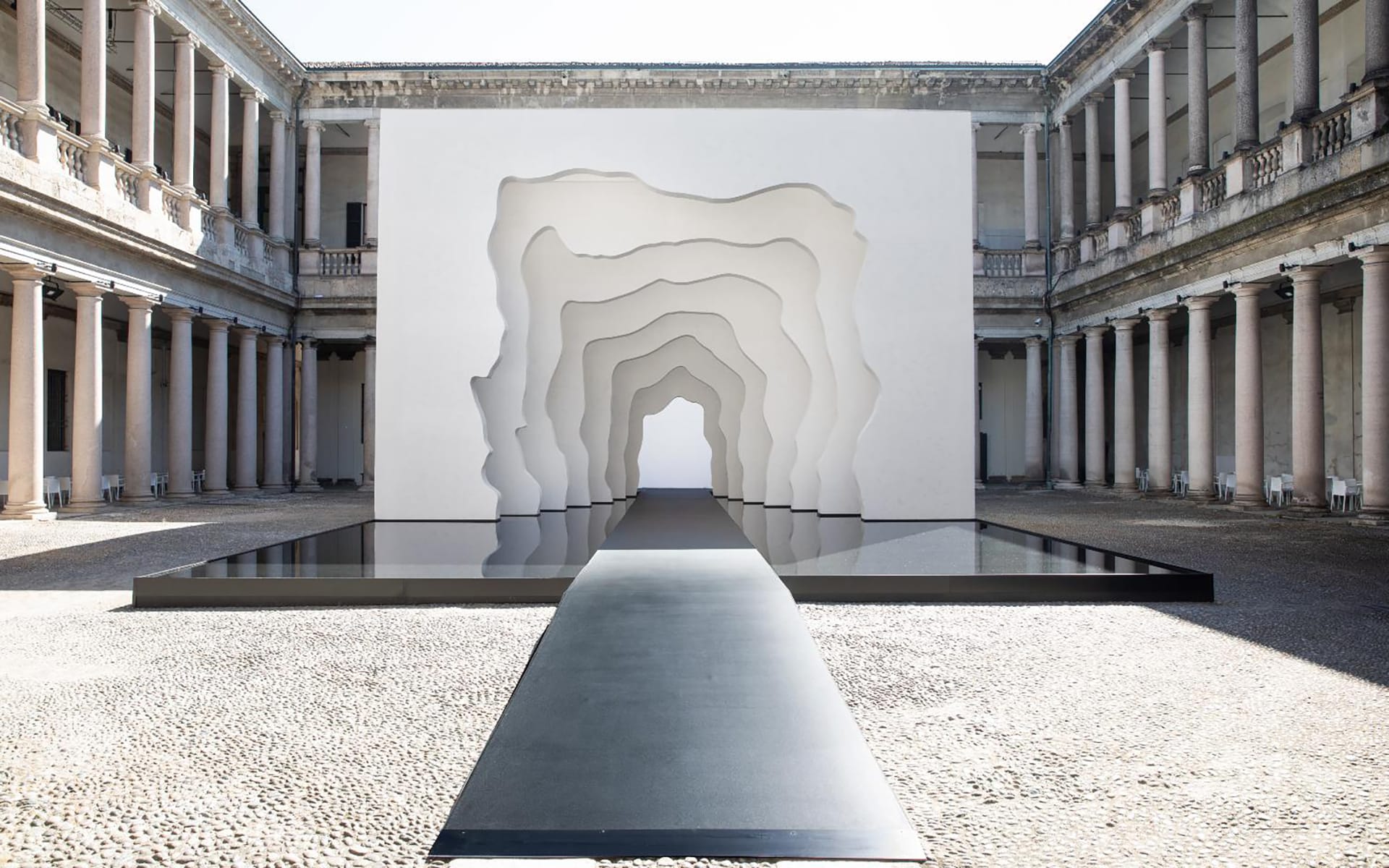 Contemporary art installation with layered arches in a rectangular courtyard, featuring classical architecture with columns.