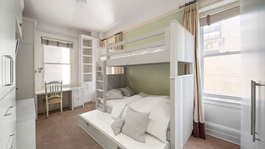 Bright bedroom with white bunk bed, pull-out trundle, built-in shelves, desk by the window, and light green accent wall.