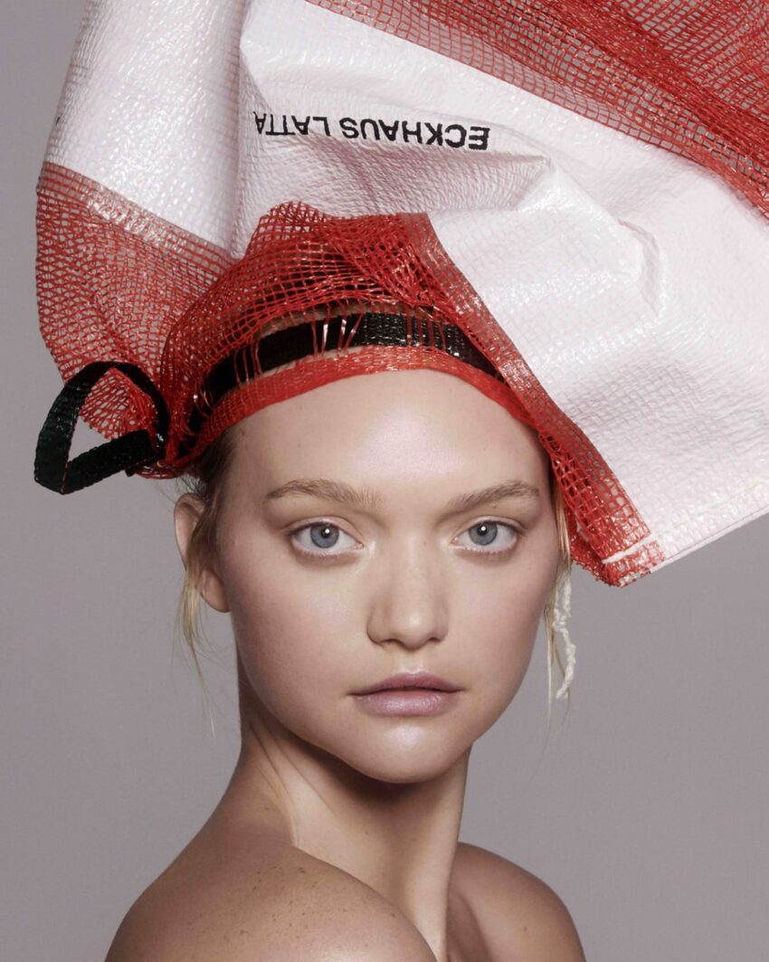 Model wearing a headpiece made of red and white textured material against a neutral background.