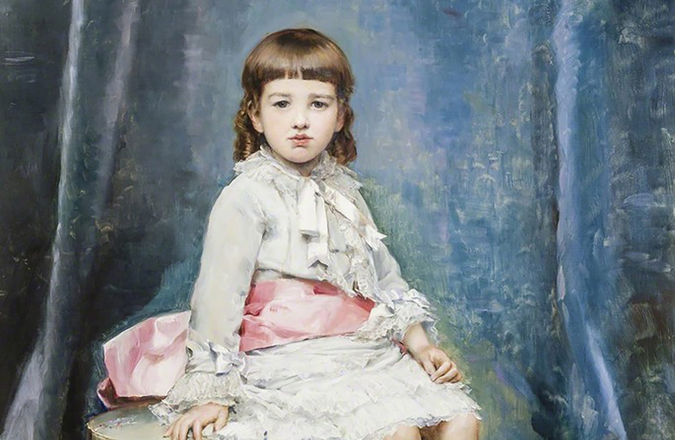 Young child in a white dress with a pink sash sits against a blue draped background, with a solemn expression.