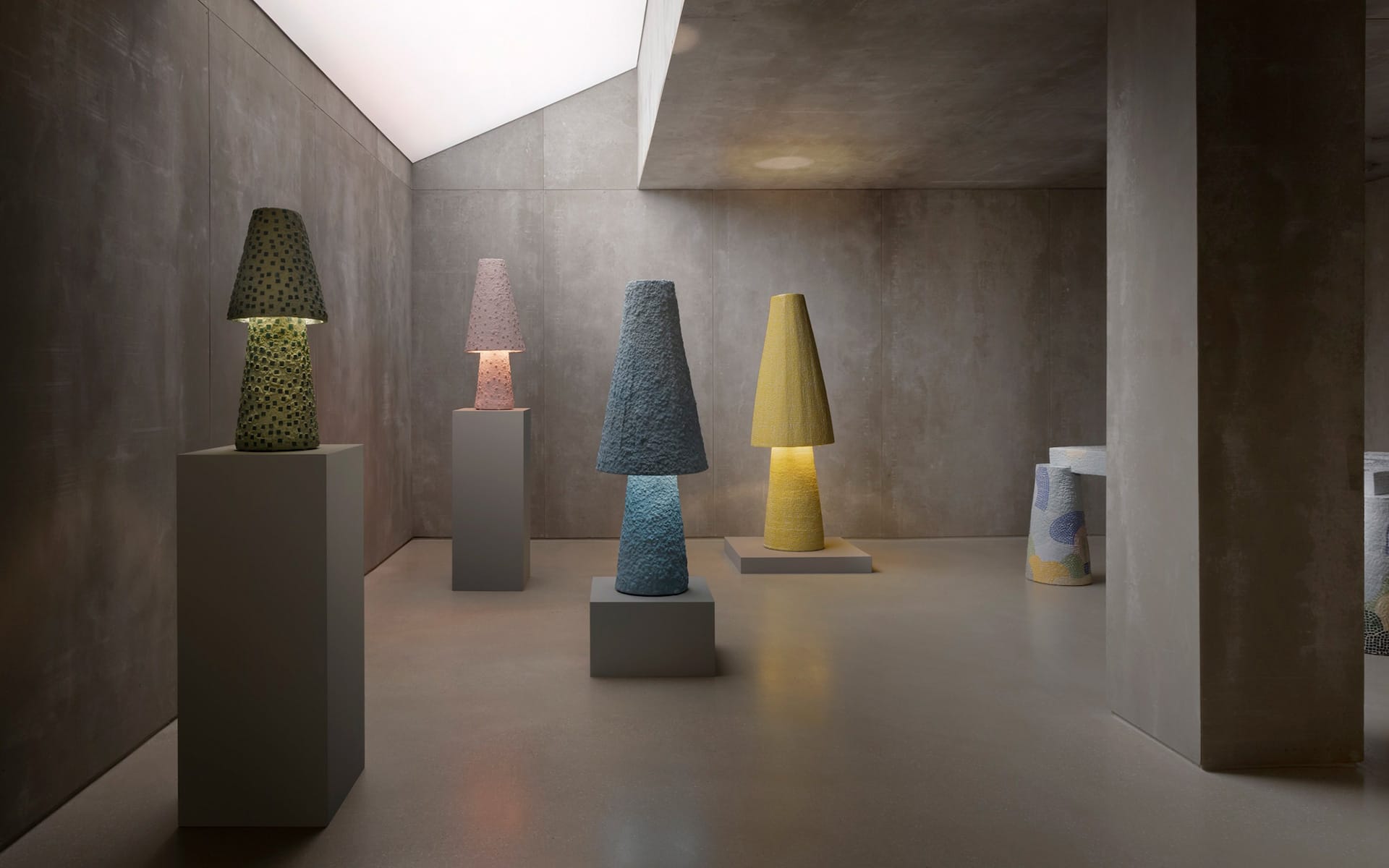 Artistic display of cone-shaped sculptures in a modern concrete gallery room with ambient lighting and pedestal stands.