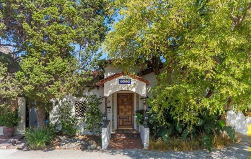 Front view of a charming house surrounded by lush greenery and trees under a clear blue sky.