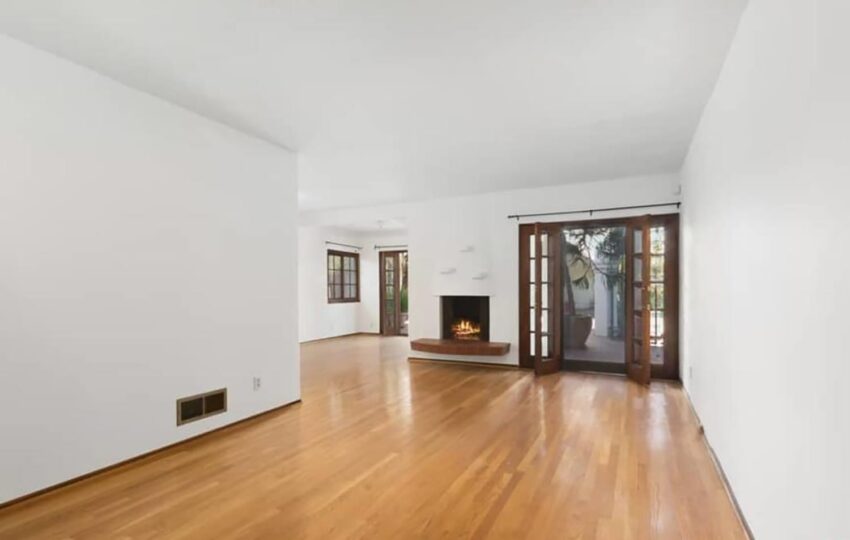 Spacious empty living room with hardwood floors, white walls, a modern fireplace, and glass doors leading outside.