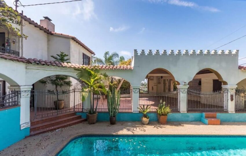 Spanish-style villa with arched patio, pool, and lush potted plants under a clear blue sky.