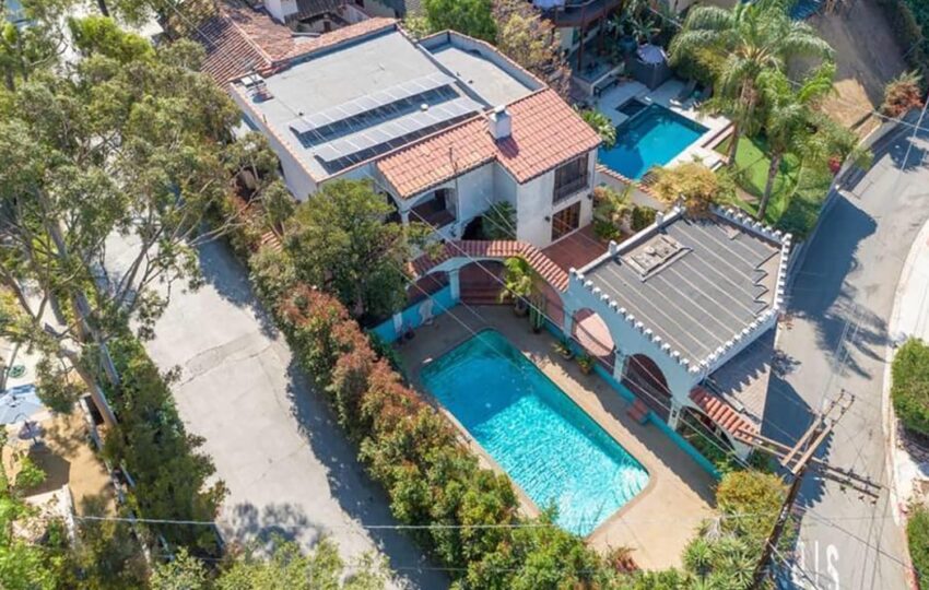 Aerial view of a house with terracotta roof, solar panels, swimming pool, and surrounding trees in a residential neighborhood.