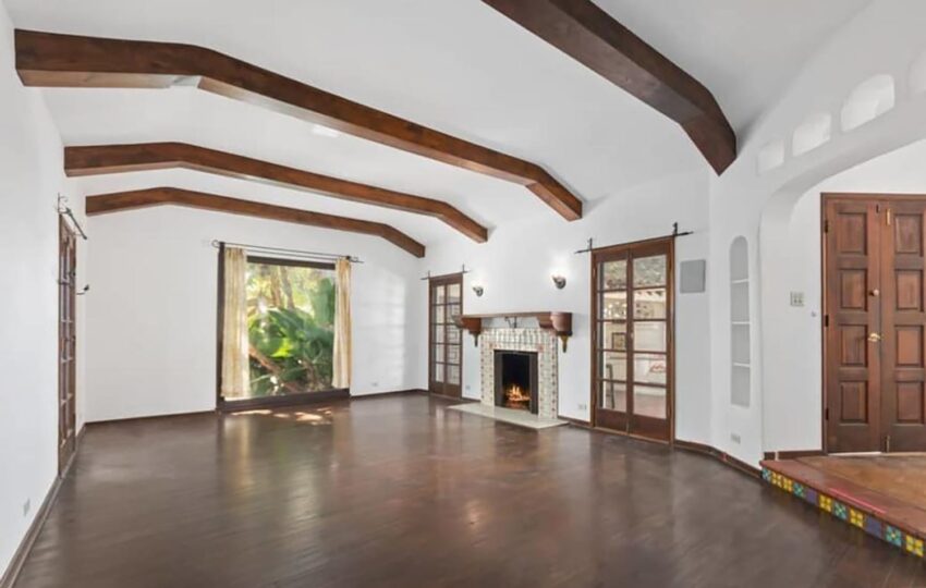 Spacious living room with wooden beams, fireplace, hardwood floors, and large windows letting in natural light.