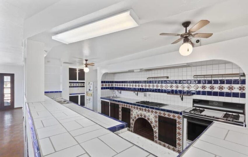 Spacious kitchen with tiled countertops, arched oven alcove, ceiling fans, and fluorescent lighting.