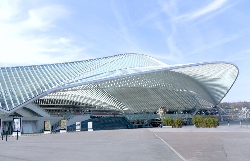 Futuristic architecture of Liège-Guillemins railway station with sweeping glass and steel design under a clear blue sky.