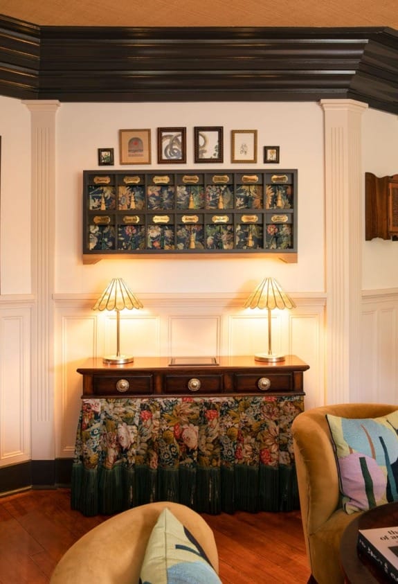 Cozy living room with a vintage sideboard, floral table skirt, two lamps, and framed prints on the wall.