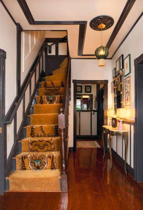 Staircase with ornate tiger-patterned carpet and framed art on the wall in a warmly lit hallway with a polished wooden floor.