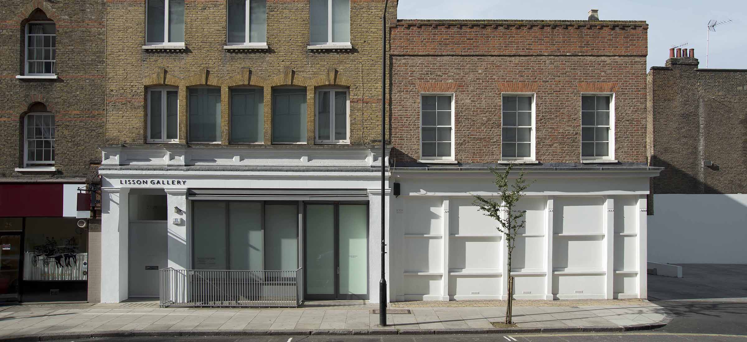 Exterior view of a gallery with a mix of modern and traditional architecture, featuring large glass windows and brick walls.