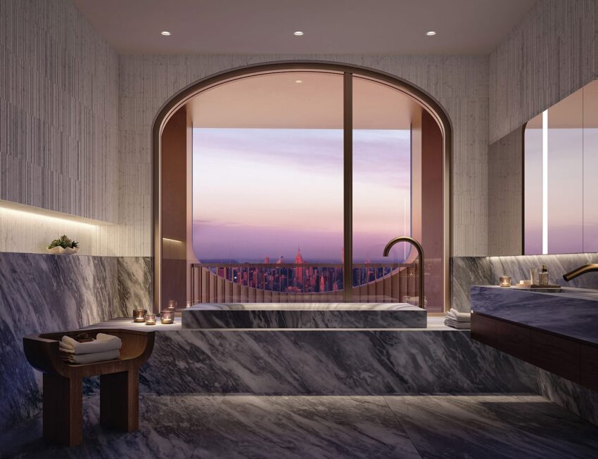 Luxurious marble bathroom with a large window view of a city skyline at sunset, candles on the tub edge.