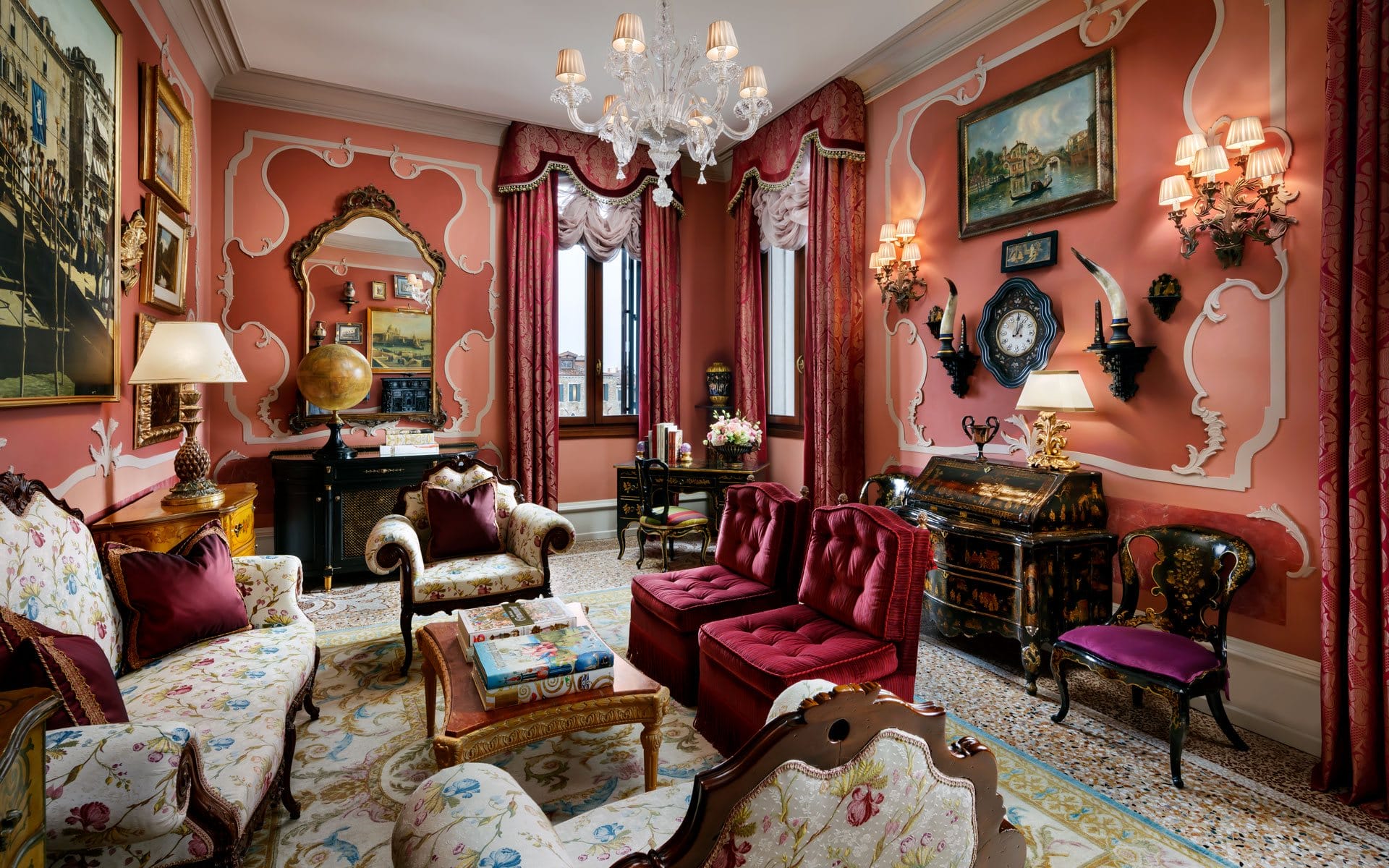 Elegant vintage living room with ornate decor, antique furniture, a globe, chandelier, and rich red and gold color scheme.
