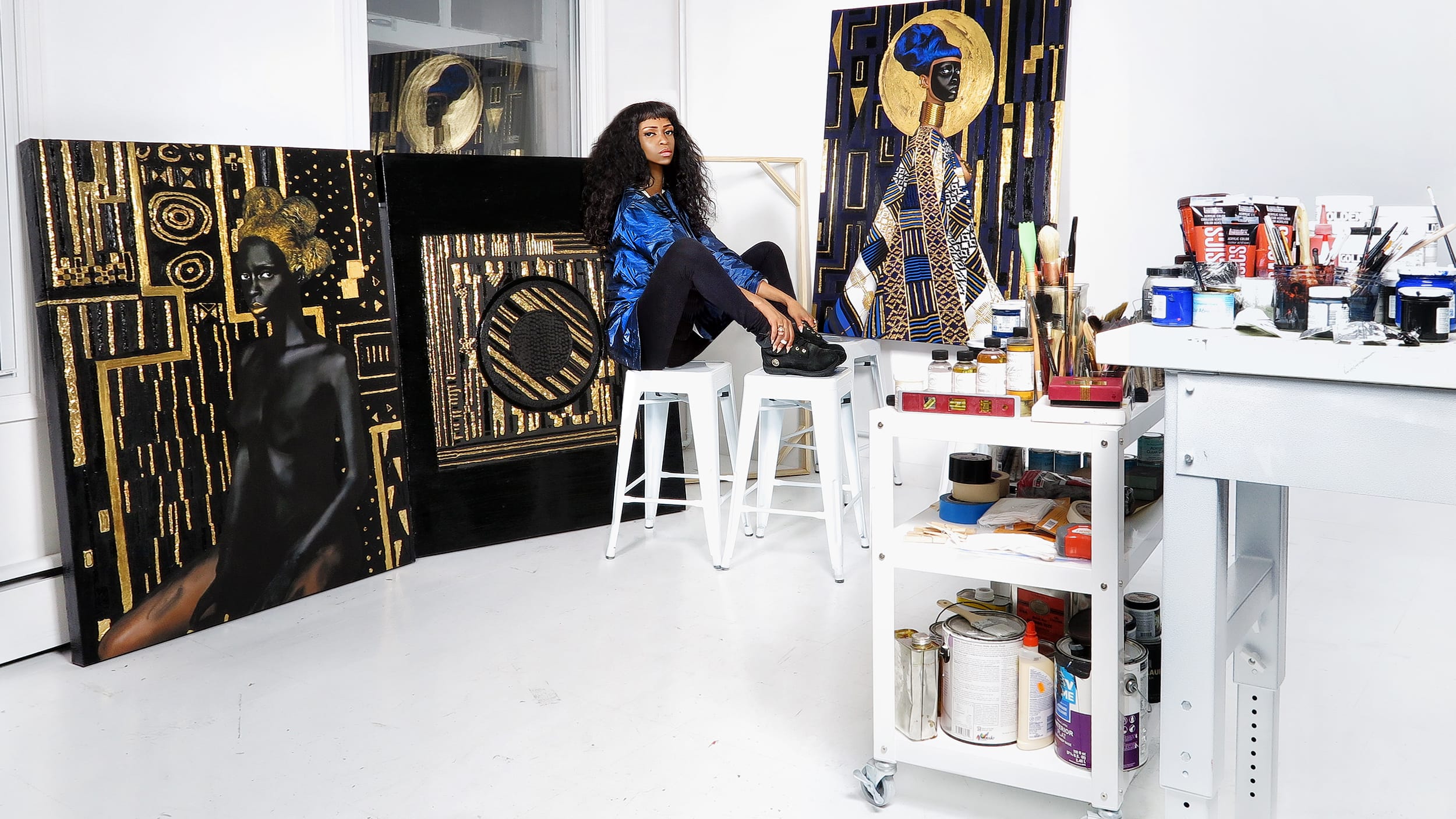 artist sitting in studio surrounded by canvas paintings and art supplies