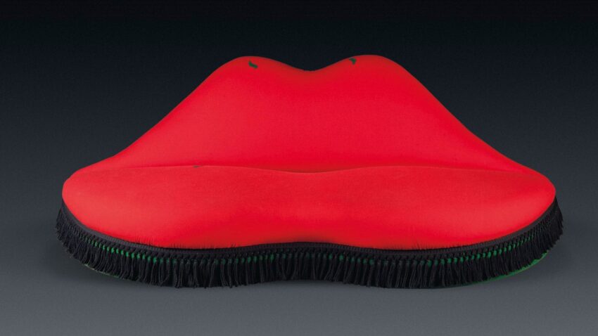 Red lips-shaped sofa with green fringed edge on a dark background.