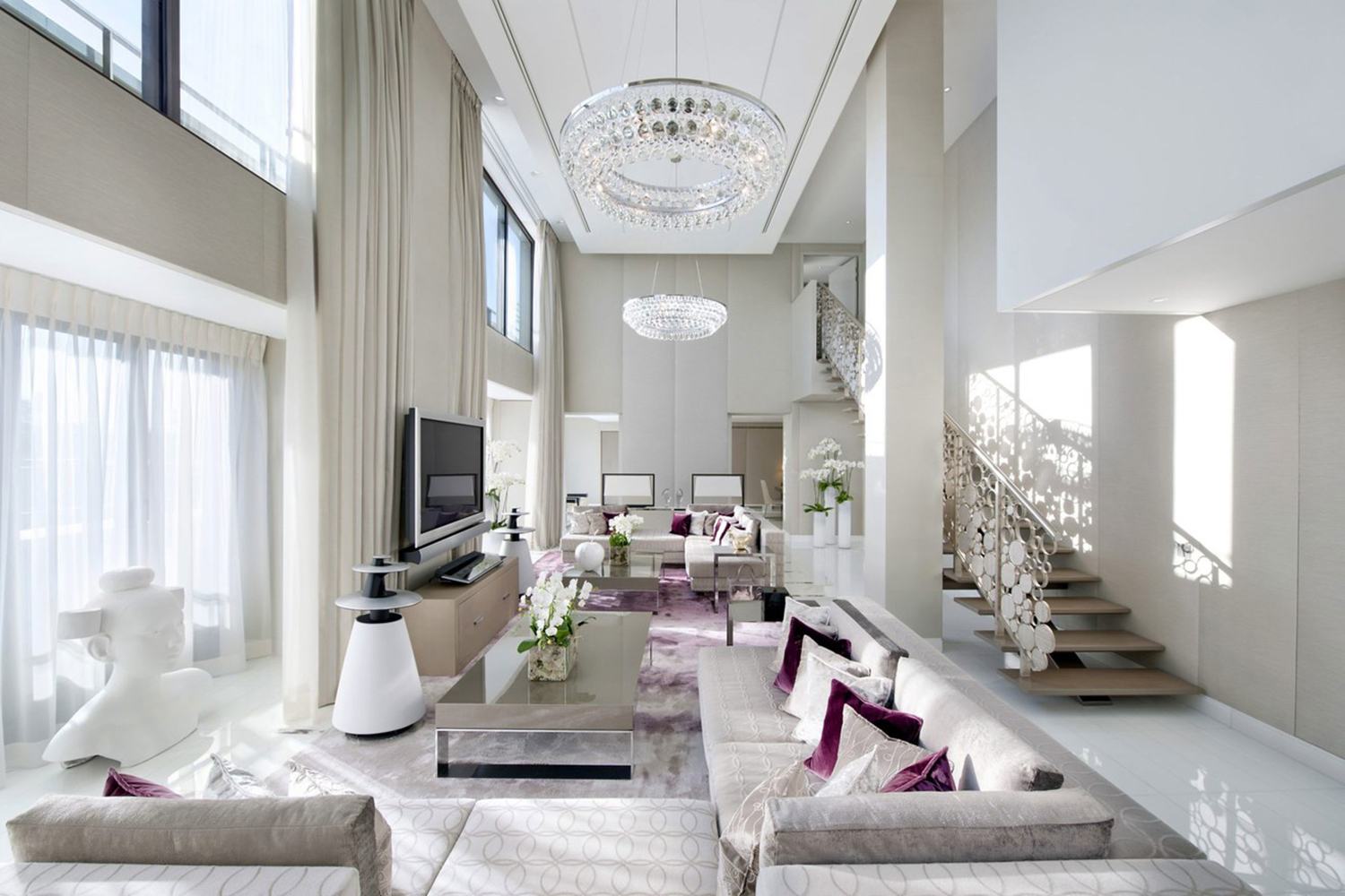 Luxury modern living room with high ceilings, elegant chandeliers, large windows, and stylish furniture in neutral tones.
