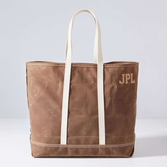 Brown canvas tote bag with white straps and JPL initials on the side, placed on a white surface against a gray background.