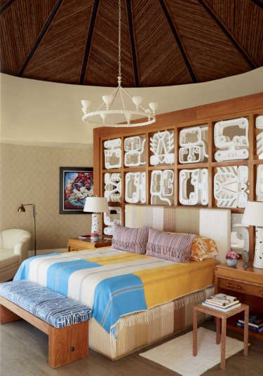 Cozy bedroom with a large bed, colorful bedding, decorative wall art, wooden ceiling, and pendant light.