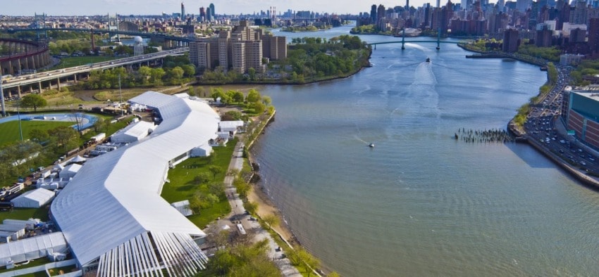 Aerial view of Randall's Island with large park, buildings, and the river, showcasing city skyline in the background.