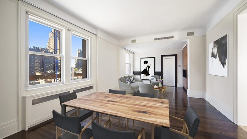 Bright modern apartment with wooden dining table, black chairs, artwork on white walls, and large windows showing a city view.