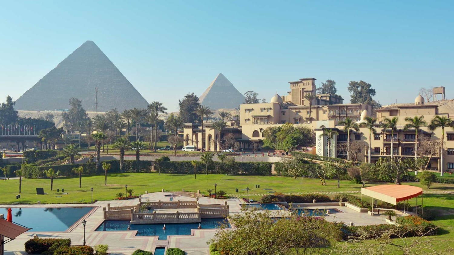 View of a hotel garden with two pyramids in the background under a clear blue sky.