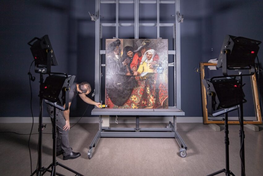 Art conservator examining a painting under studio lights with equipment in a controlled environment.