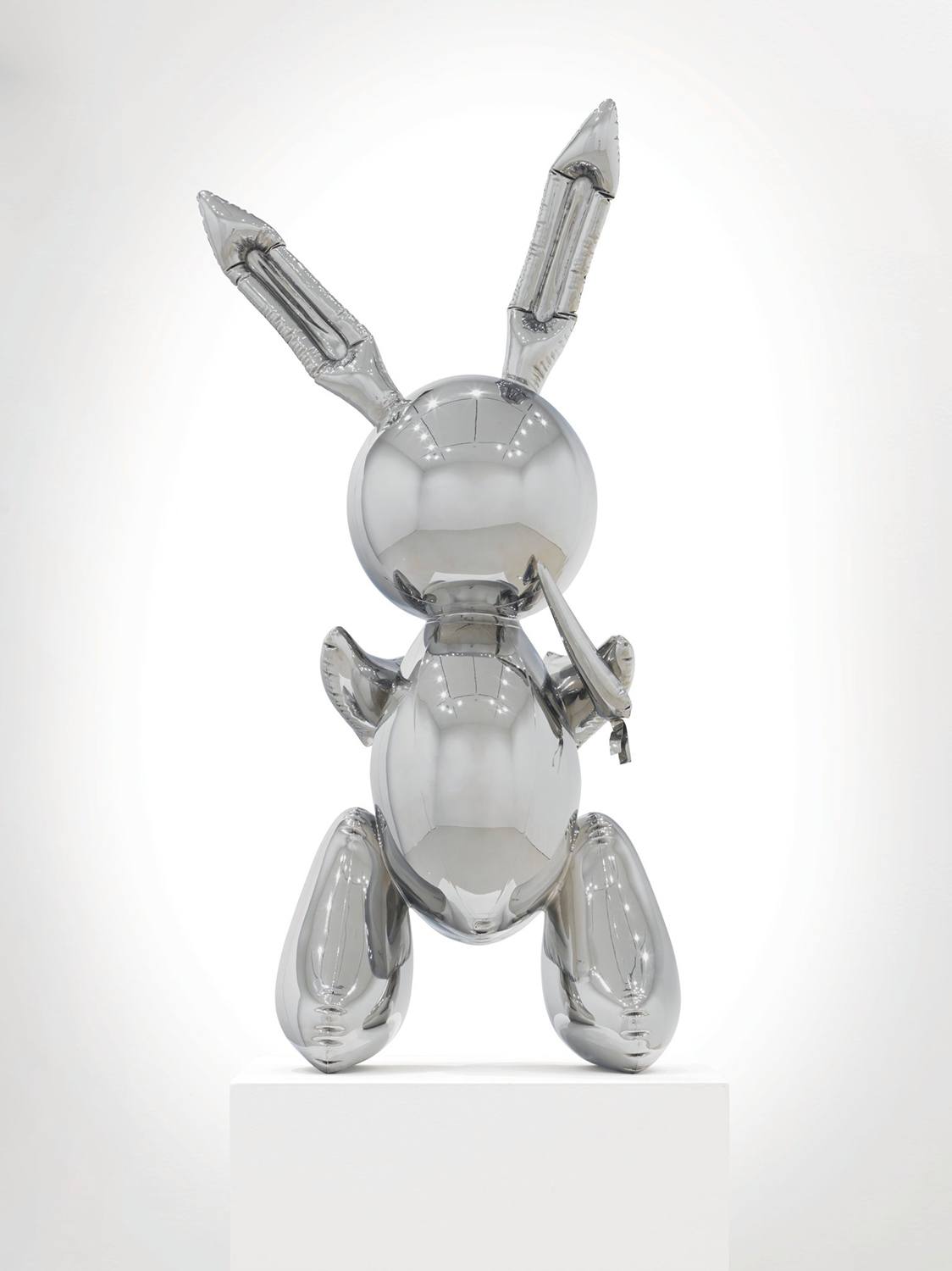 Metallic sculpture of a reflective bunny with long ears, displayed on a white pedestal.