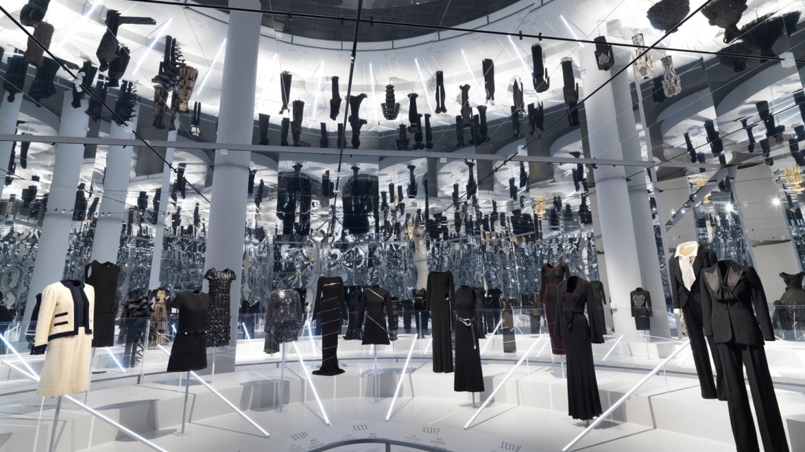 Fashion exhibition with various black and white outfits displayed in a reflective room with mirrored ceiling and walls.