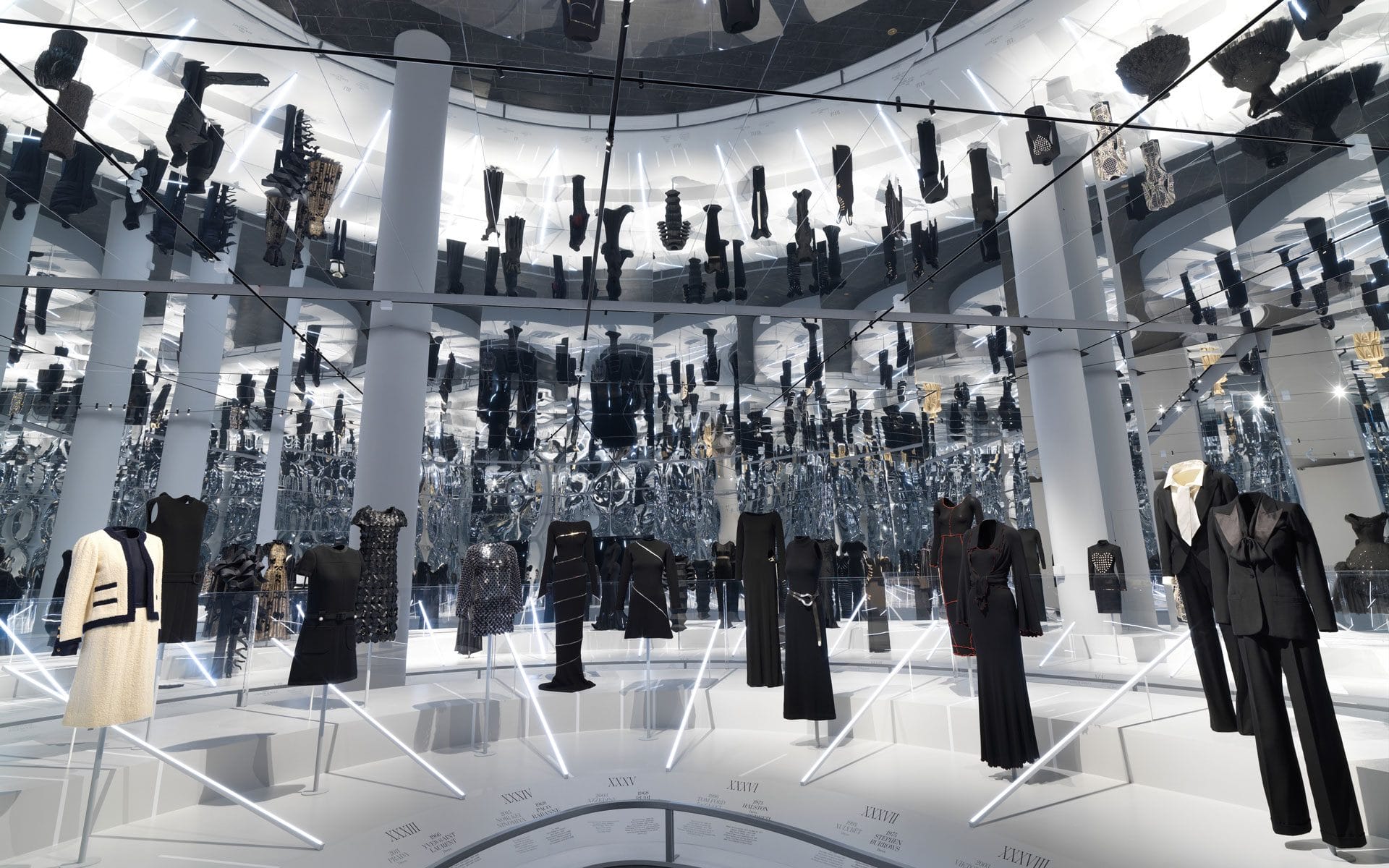 Fashion exhibition with various black and white outfits displayed in a reflective room with mirrored ceiling and walls.
