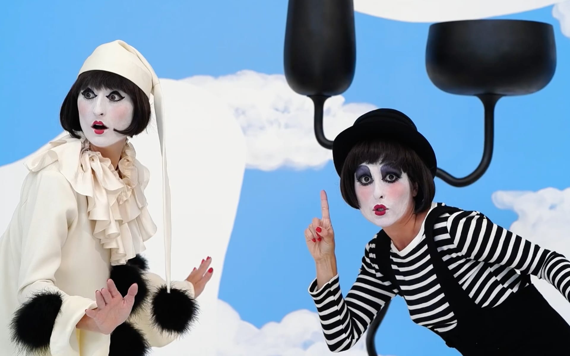 Two mime performers in playful poses with a whimsical background of blue sky and clouds.