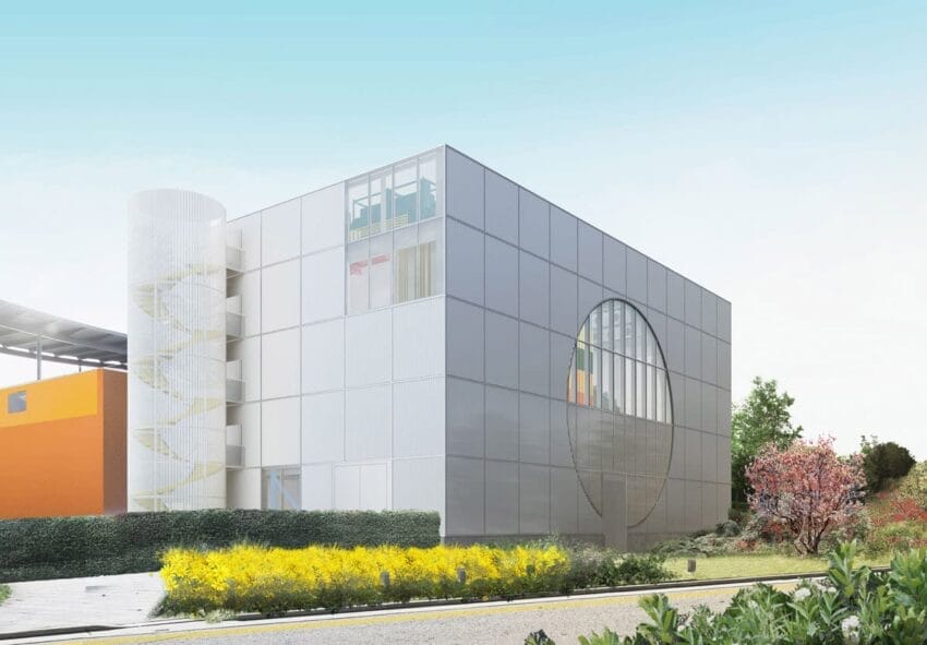 Modern building with glass facade, circular window, and floral landscape under a clear blue sky.