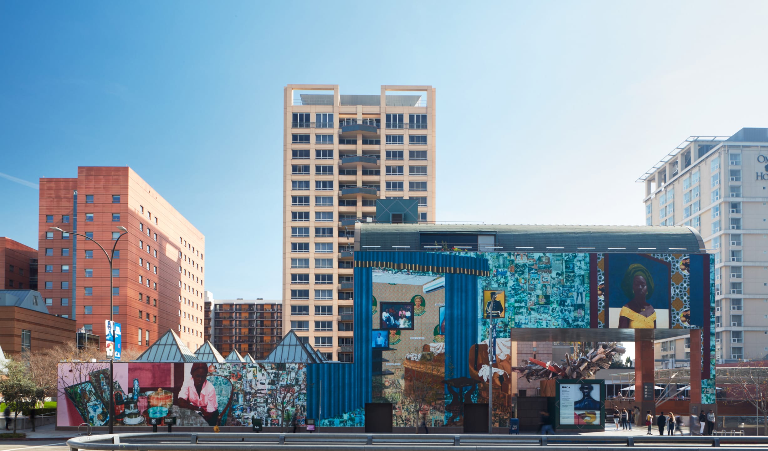 Urban street art murals on building facade with colorful patterns and portraits, set against a backdrop of modern city architecture.