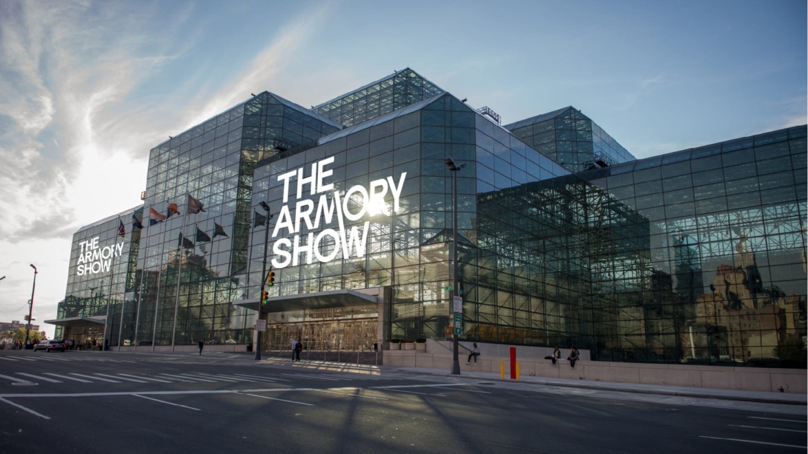 Exterior view of The Armory Show building, with large glass windows and signage against a blue sky background.