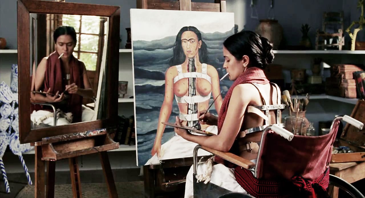 Artist painting a self-portrait while sitting in front of a mirror, wearing a back brace and a scarf in a studio setting