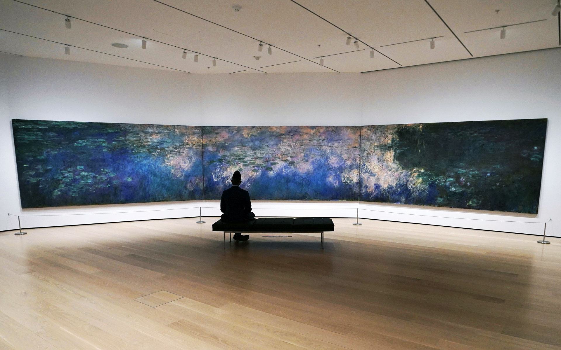 Person sitting on a bench viewing a large triptych of Claude Monet's Water Lilies in an art gallery.